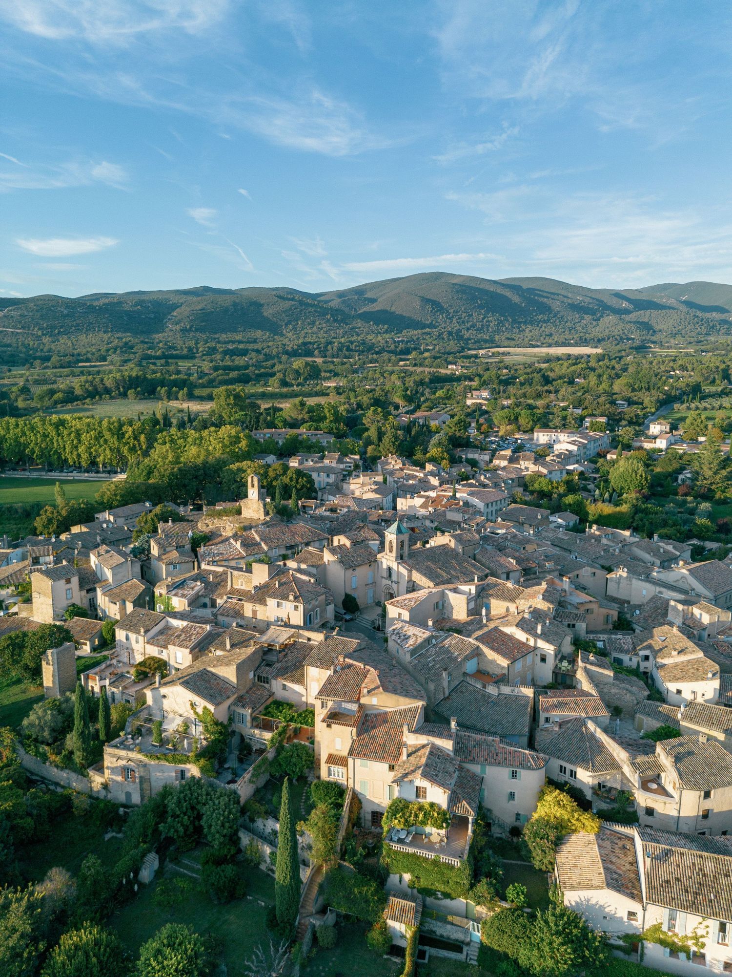Aerial panoramic view of a historic Mediterranean village nestled in rolling hills with traditional stone buildings and church.