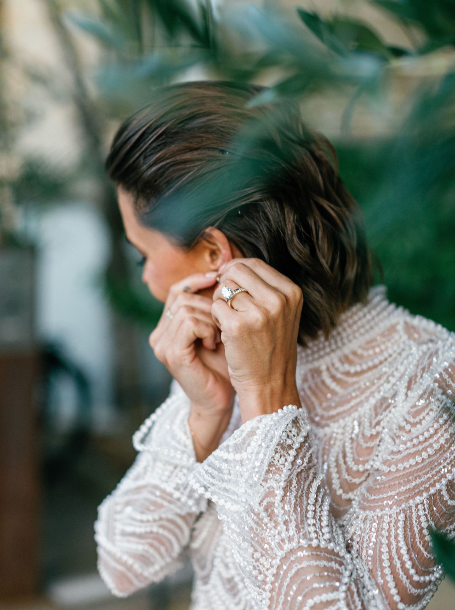 Person wearing an elegant white lace high-neck dress poses with hand covering face in a dreamy outdoor setting.