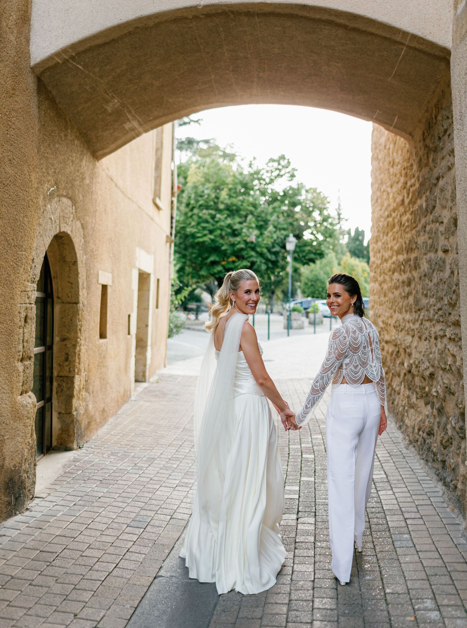 A series of archway photos showing two people in white dresses walking and holding hands along a stone corridor.