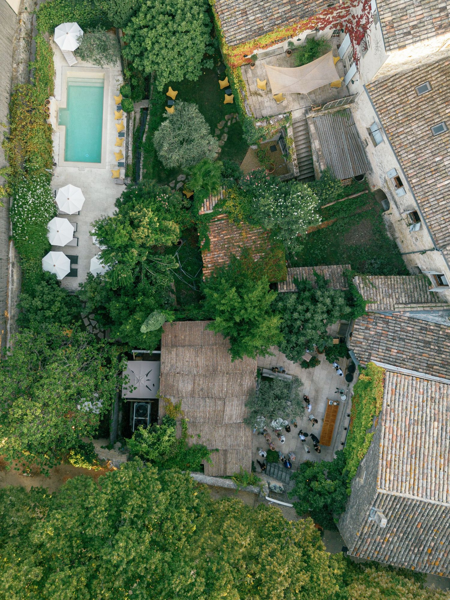 Aerial drone view of traditional stone buildings with terracotta roofs surrounded by lush Mediterranean gardens.