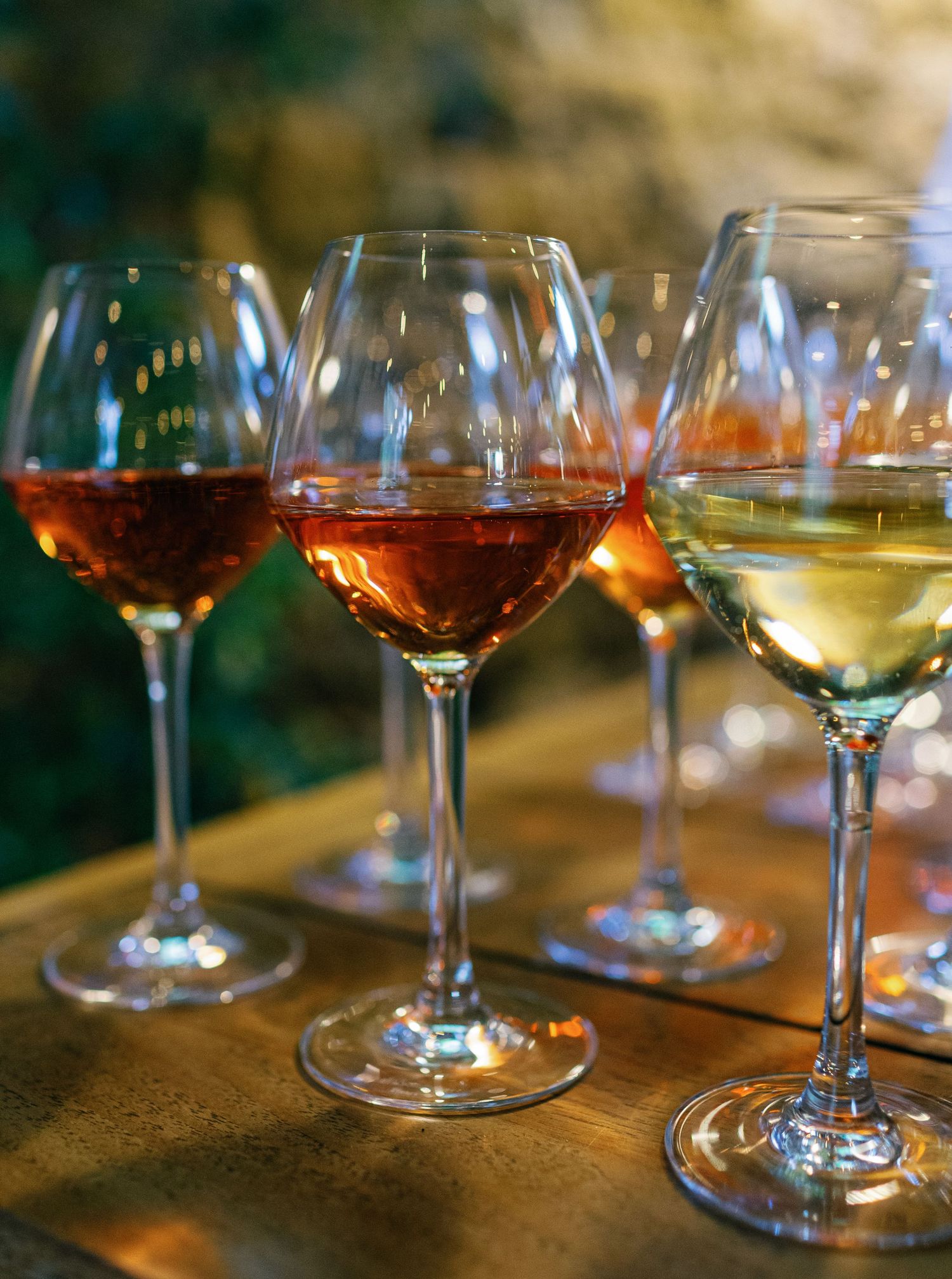 Several wine glasses filled with red and white wines sit on a wooden surface in warm lighting.