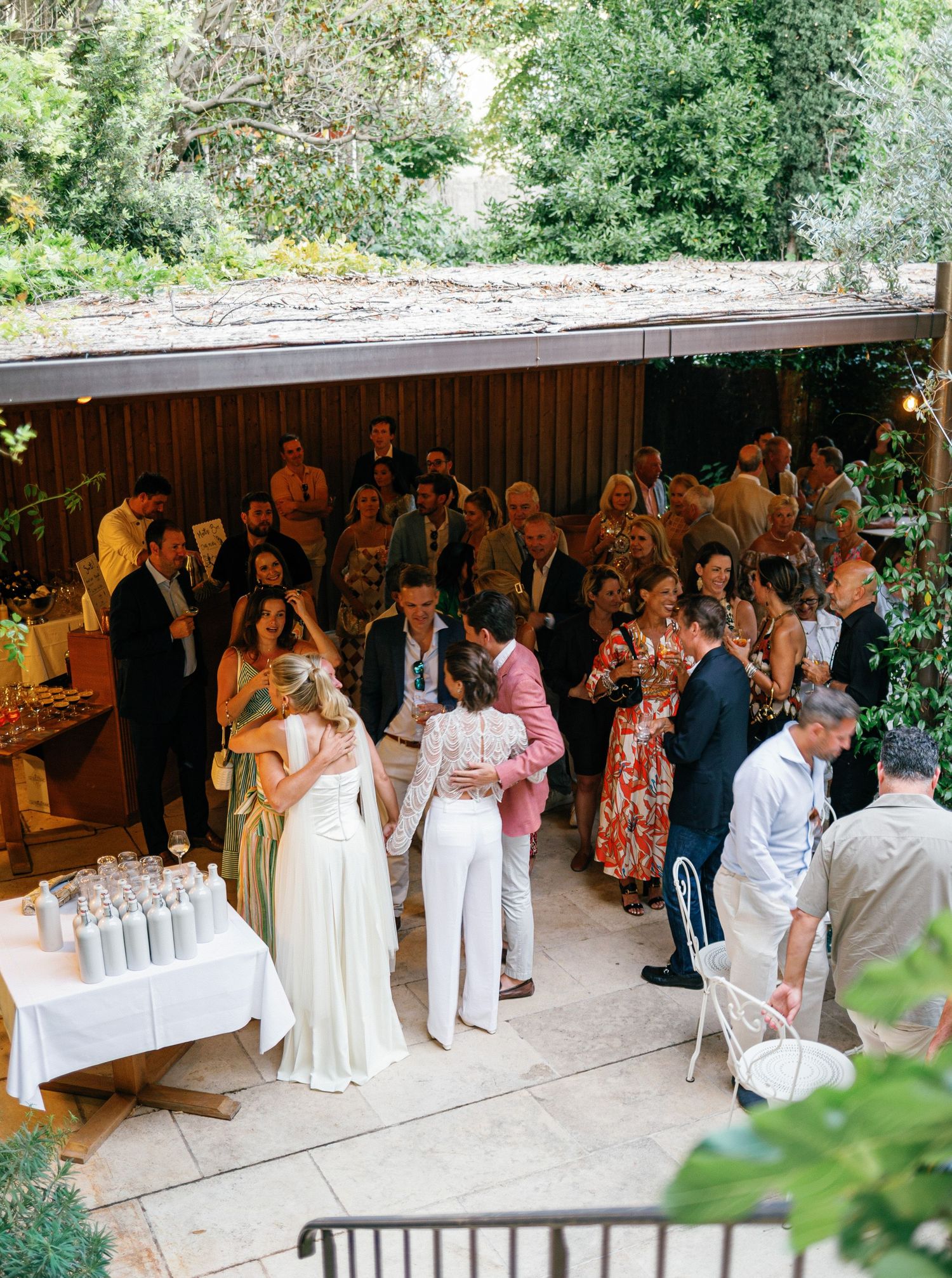 Wedding guests gather at an outdoor reception venue with string lights and refreshment tables.