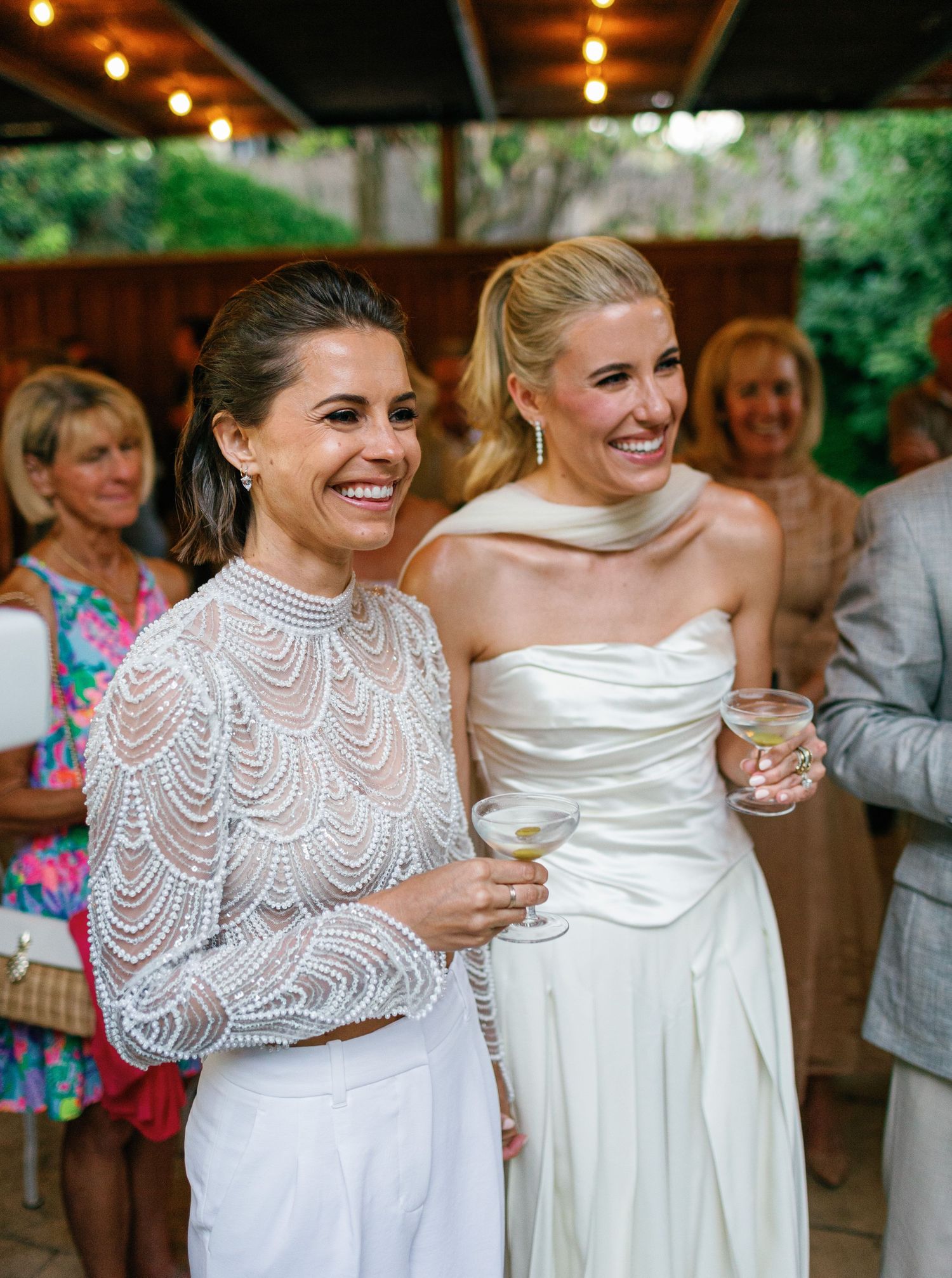 Wedding party members in white dresses share a joyful moment at an evening celebration.