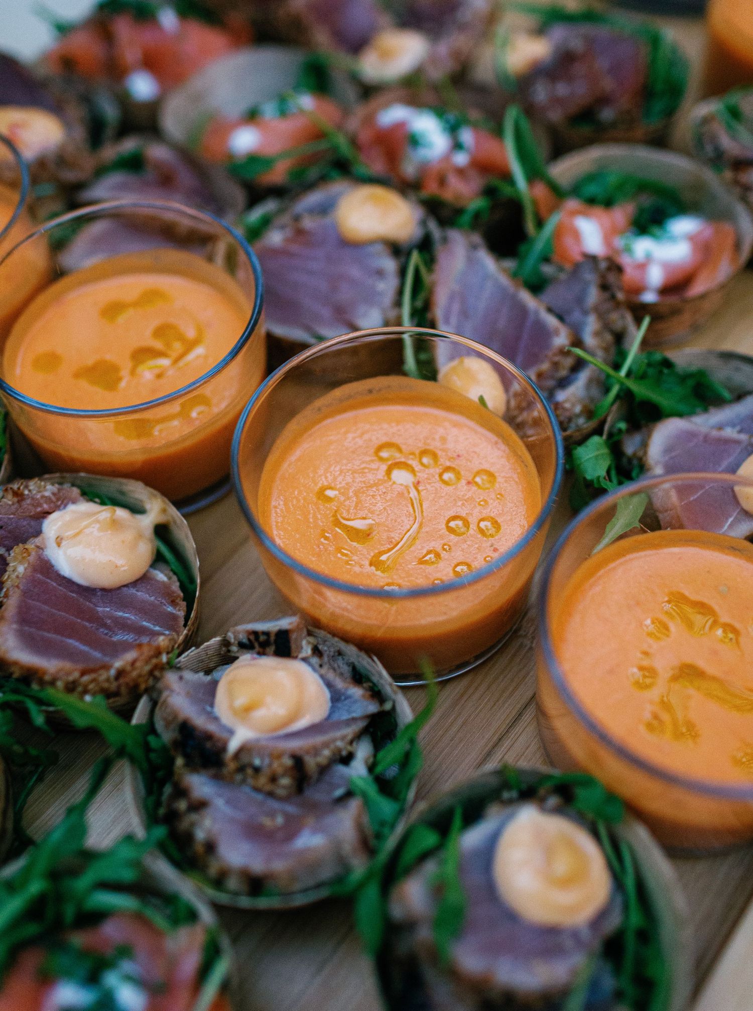 Orange creamy sauce in small glass bowls served alongside meat appetizers and fresh herbs on a wooden surface.