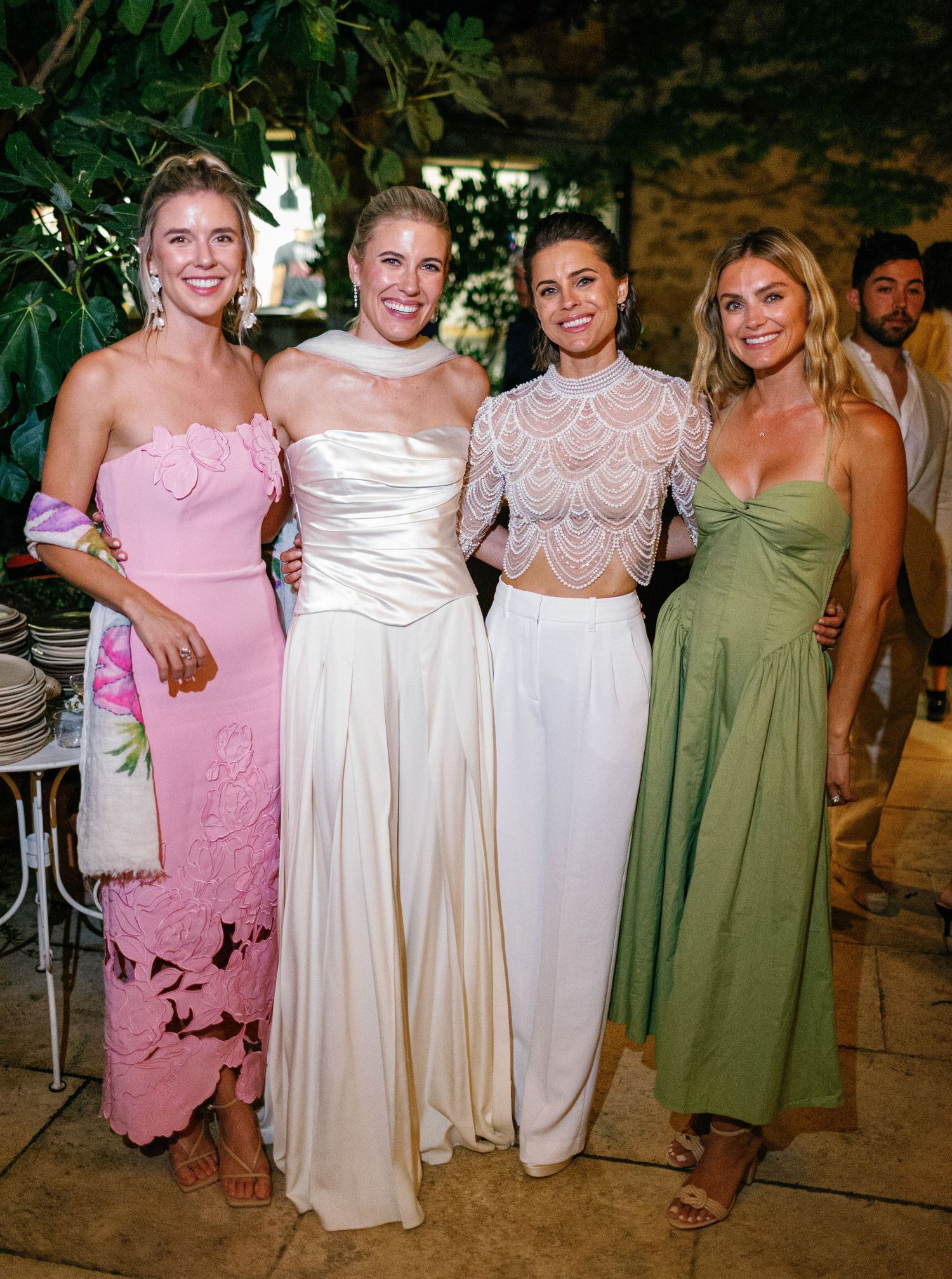 Bridesmaids pose together in coordinating pink, cream and sage green dresses at a wedding celebration.