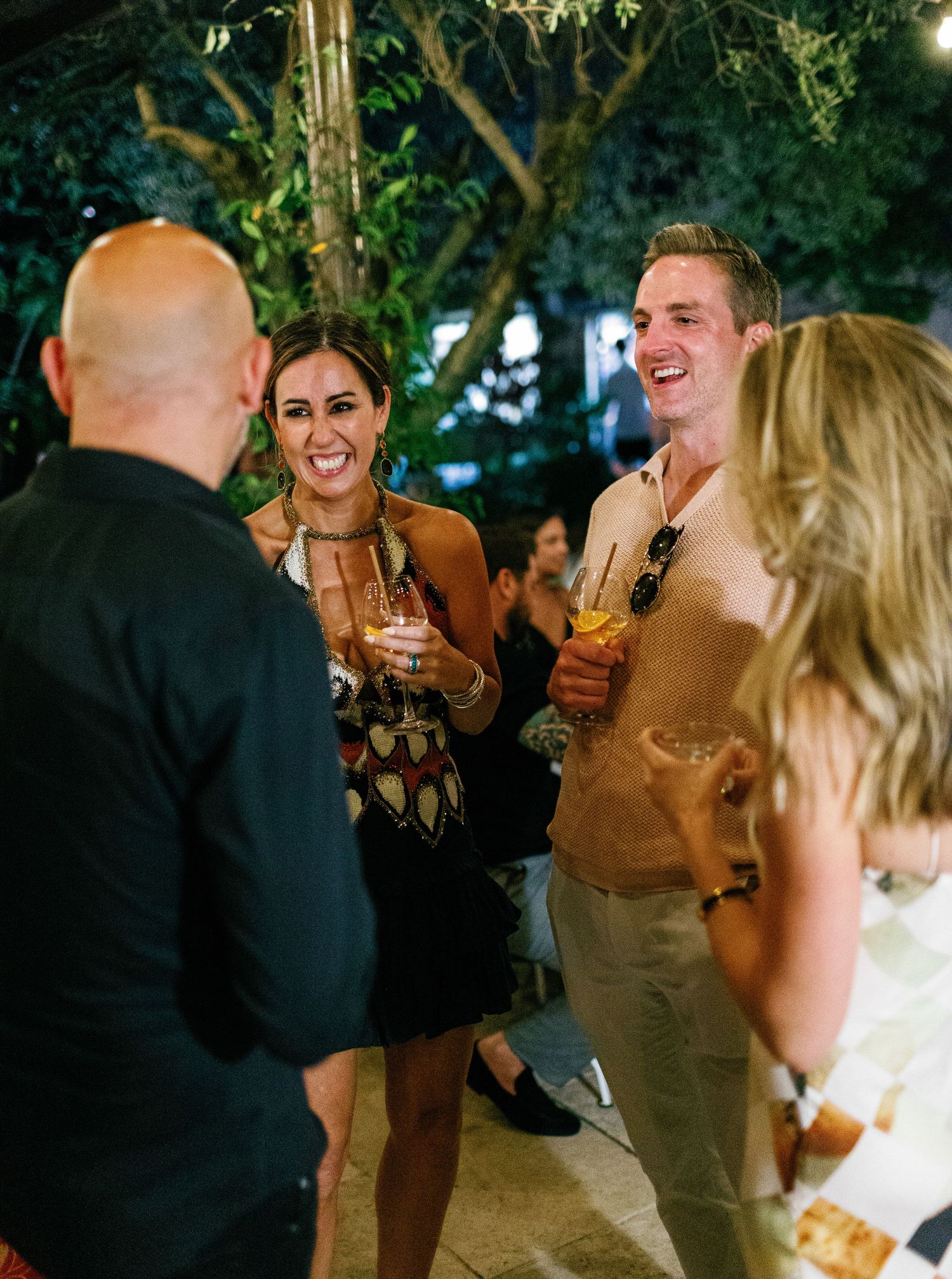 A group of wedding guests enjoying drinks and conversation at an outdoor evening reception.
