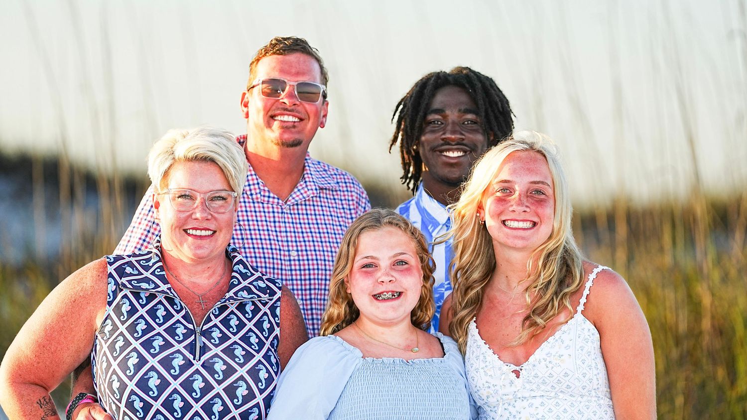 Family of five smiling together at golden hour on a beach, posing for a portrait photo.