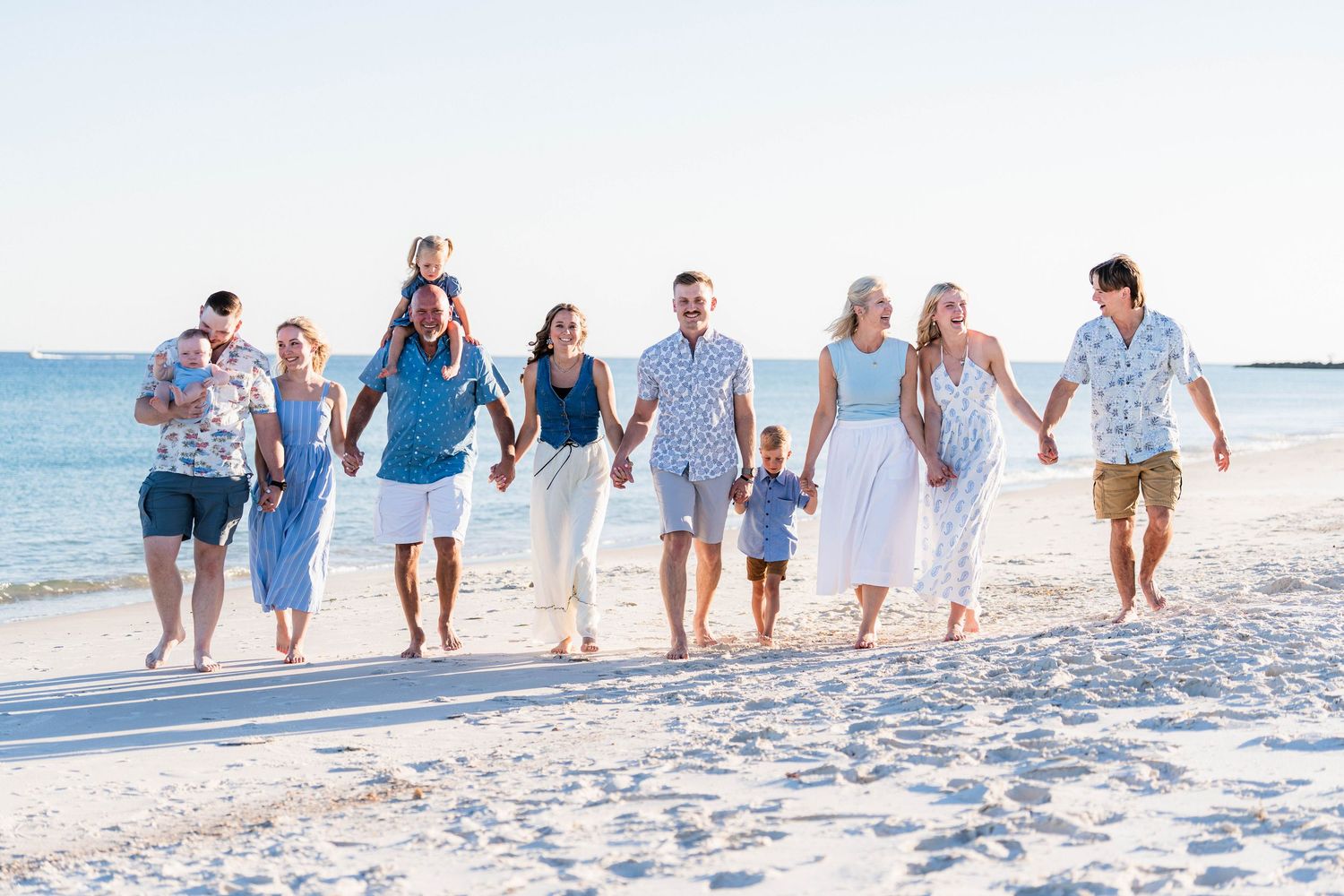 Large family group walking together on a sunny white sand beach, dressed in coordinating blue and white outfits.