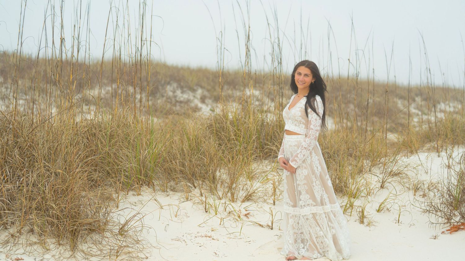 Artistic beach photography session with flowing white dress against coastal landscape.