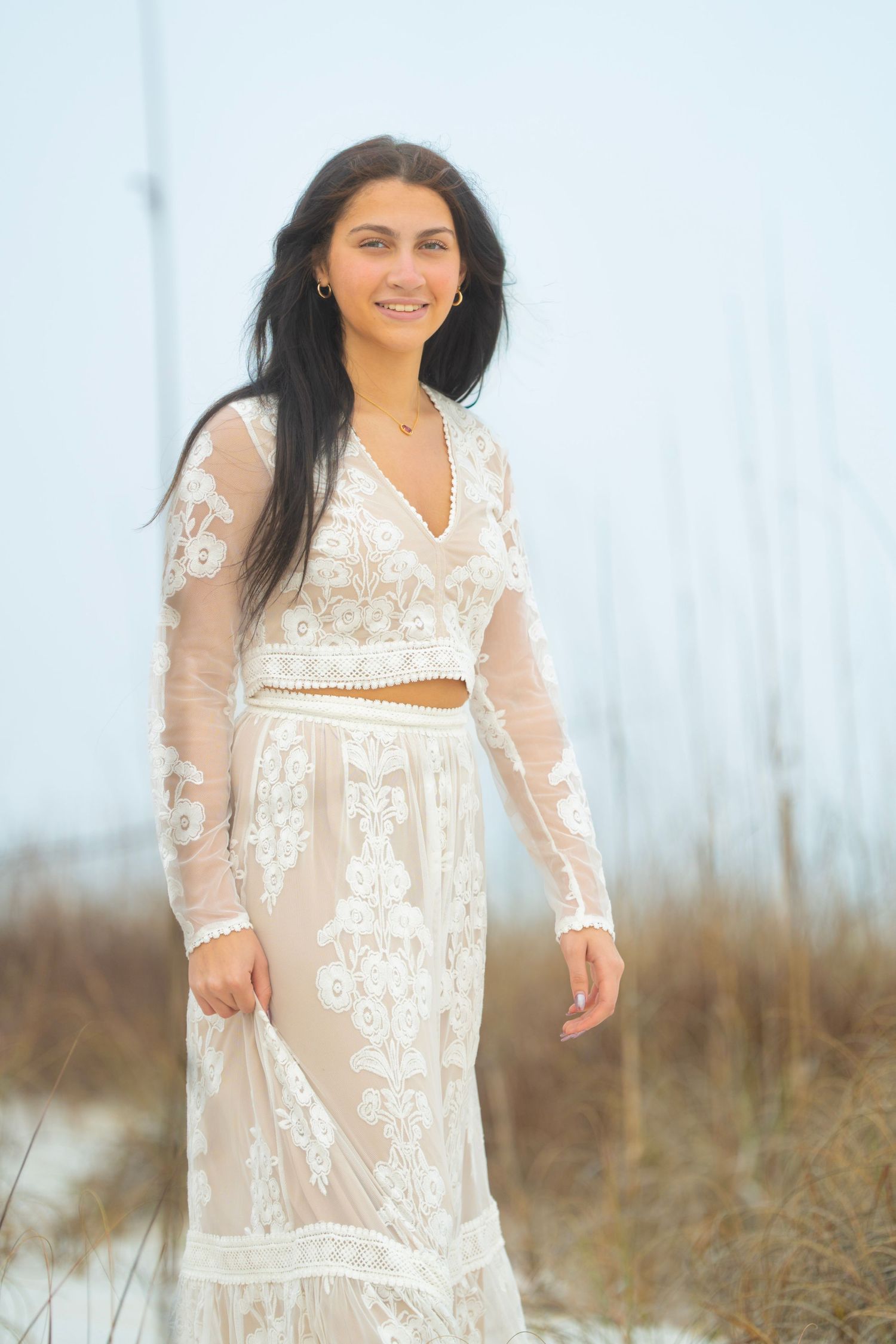 Romantic beach photography featuring flowing white lace dress against coastal grasses.