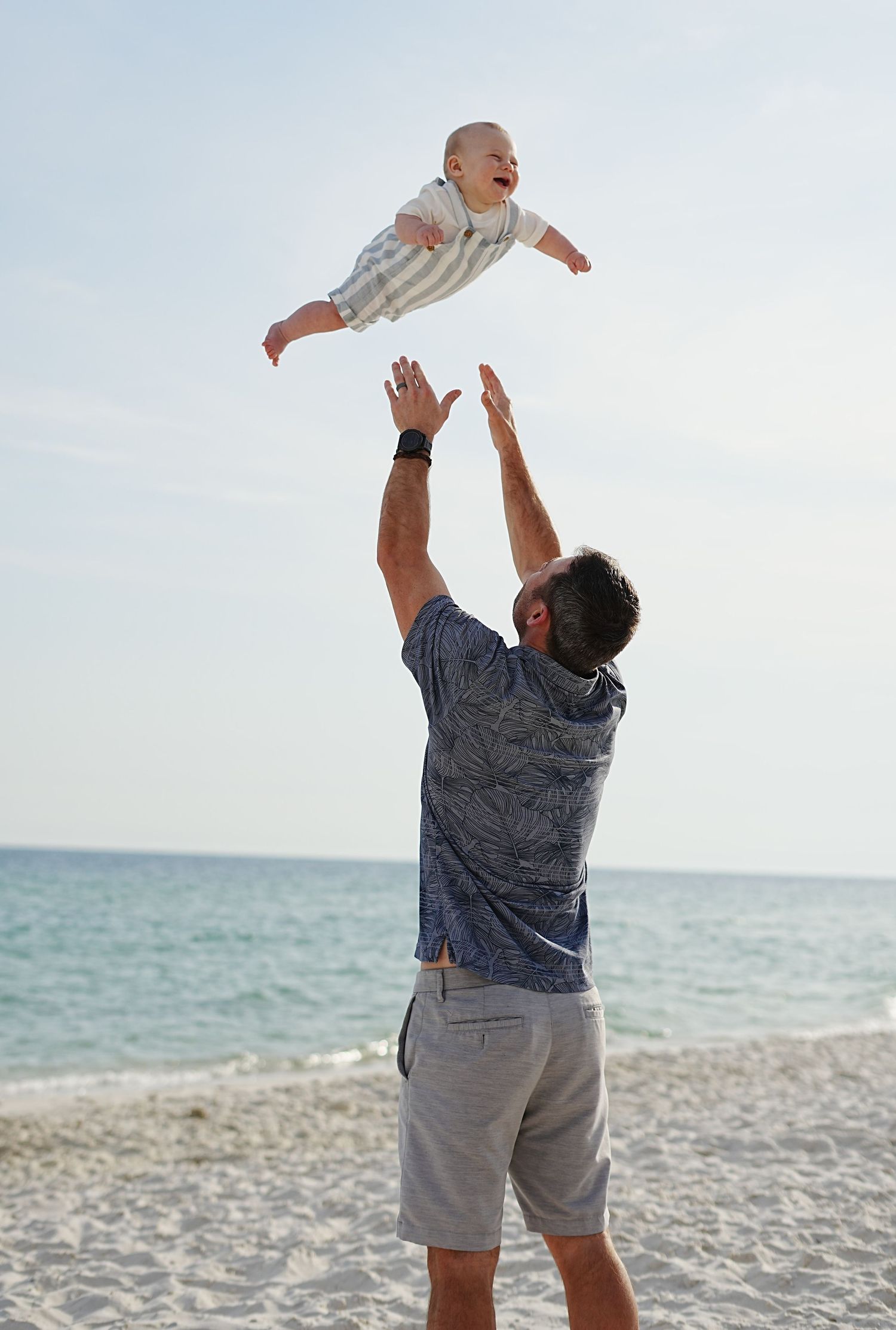 A sequence of joyful moments showing a person tossing a baby in the air at the beach while playing together.