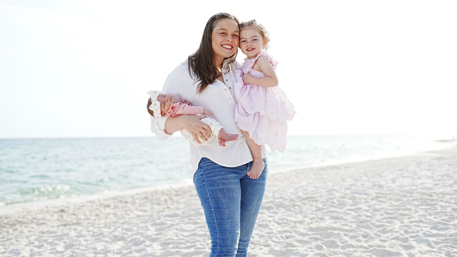 A family walks together along a sunny beach wearing casual clothing and enjoying a warm summer day.