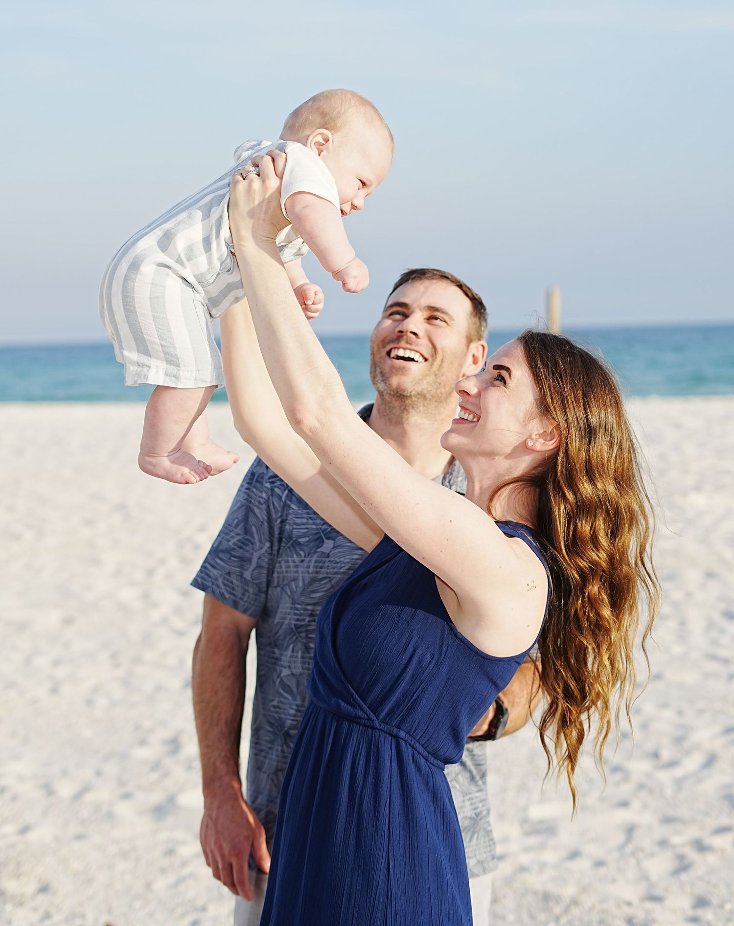 Family enjoying a playful moment together on a pristine white sandy beach with ocean views in the background.