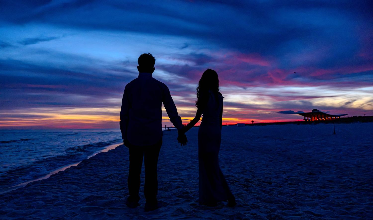 Silhouette of a couple holding hands on a beach at sunset with vibrant blue and orange sky.