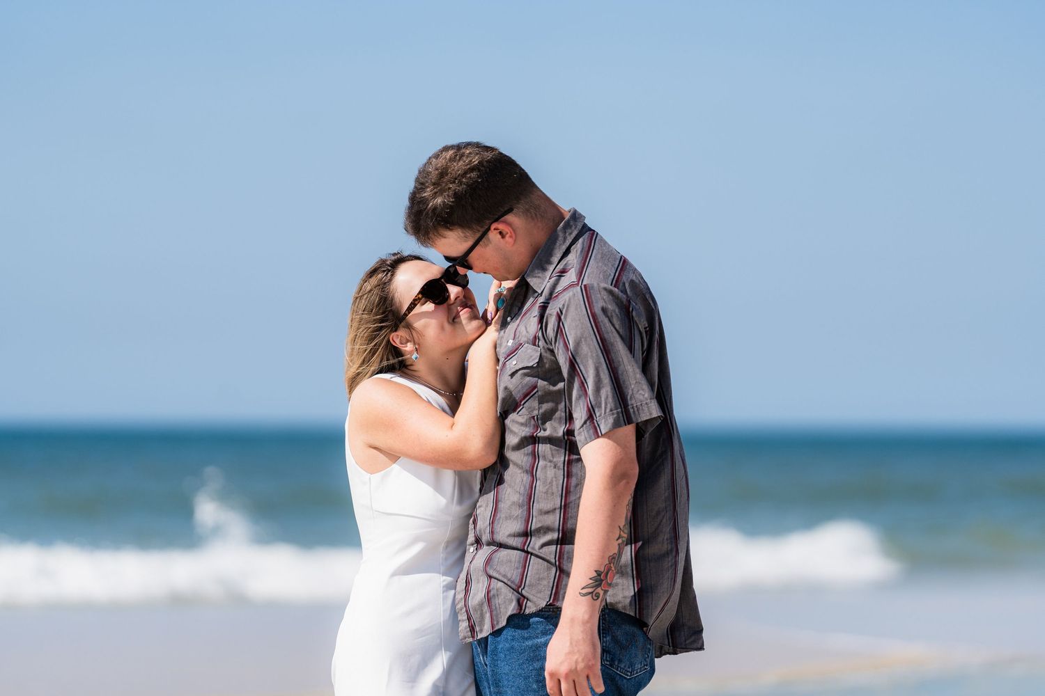 Couple sharing a romantic moment on a sunny beach with ocean waves in the background.