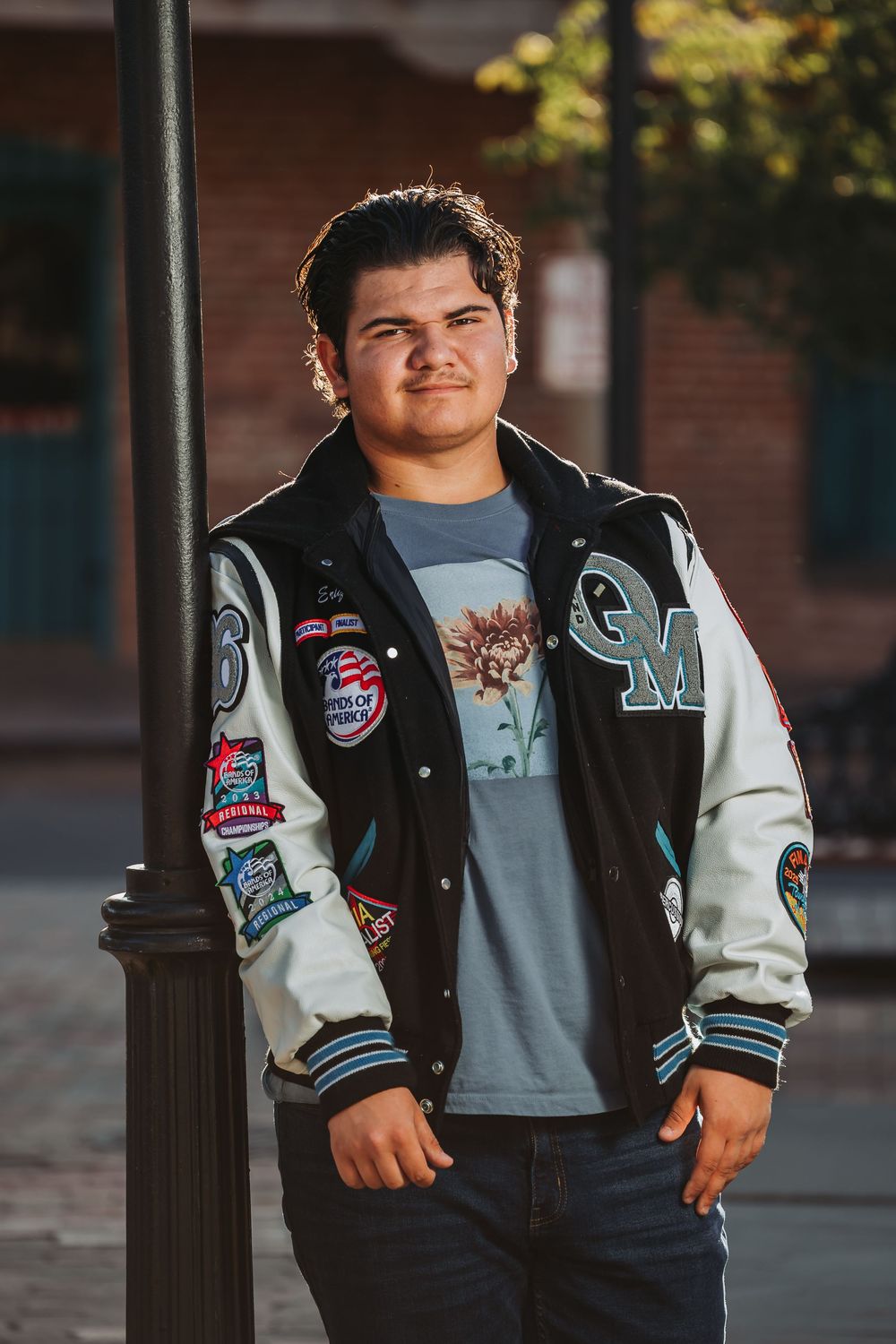 A varsity letterman jacket with patches and emblems is worn casually with jeans and a t-shirt in an outdoor setting.