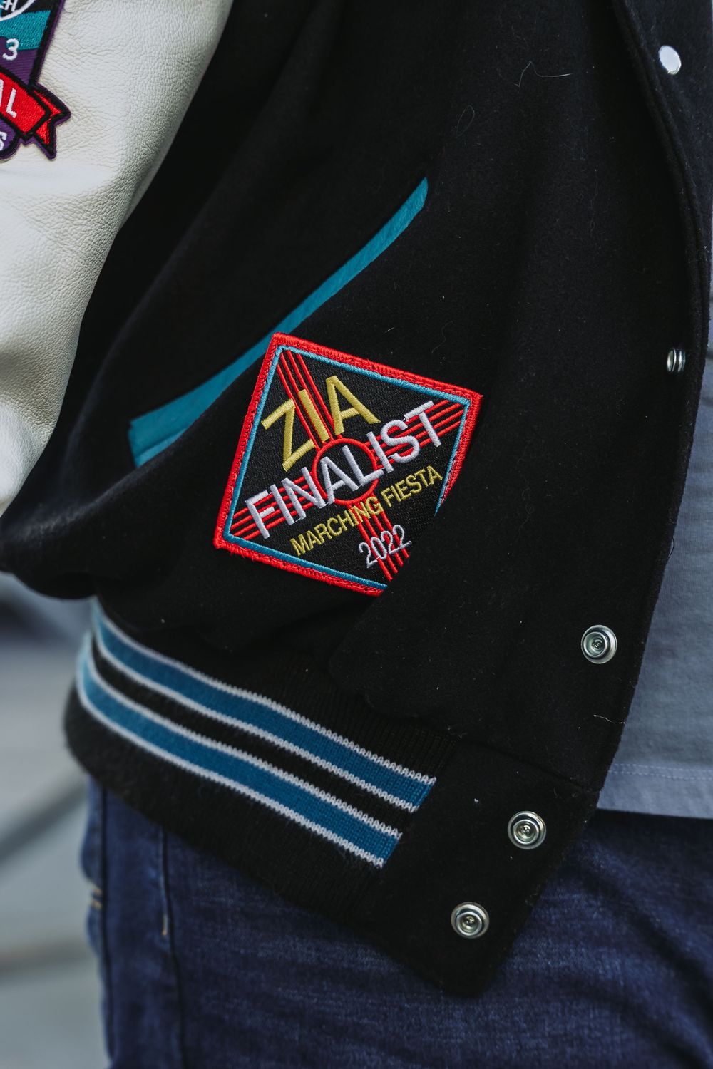 Close-up view of a black varsity jacket with colorful embroidered patches and silver snap buttons.