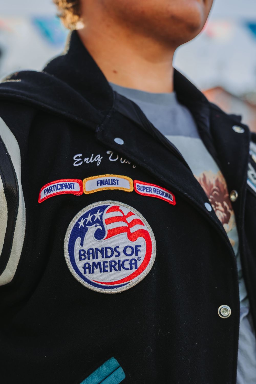 Close-up of Bands of America patch and achievement badges on black varsity jacket.