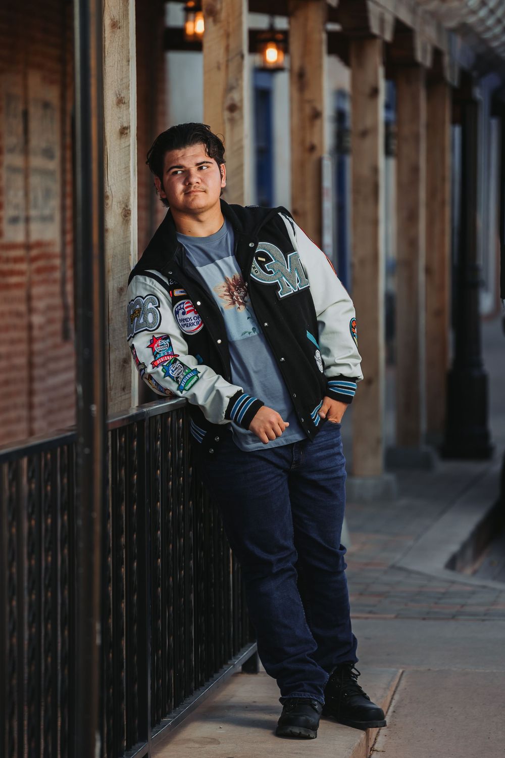 A person in a denim vest and jeans poses in a rustic hallway with stone columns and lantern lighting.