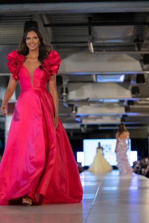 Vibrant hot pink ballgown with ruffled sleeves flows down fashion runway.
