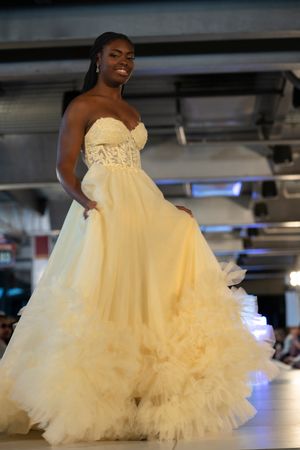 Fashion model showcases voluminous cream tulle ballgown on illuminated runway.