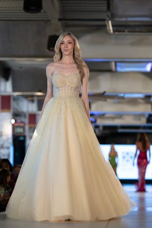 Model showcasing an elegant ivory ball gown with corset bodice and tulle skirt on the catwalk.