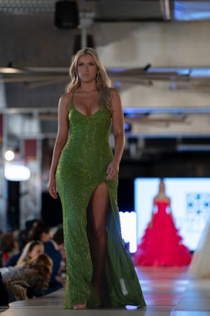 A sequined emerald green evening gown with a high slit being presented on a fashion catwalk.