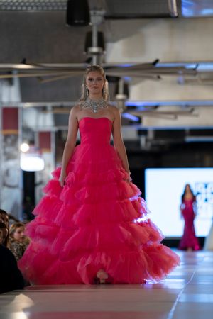 Model walks runway in voluminous hot pink tulle ball gown during fashion show.