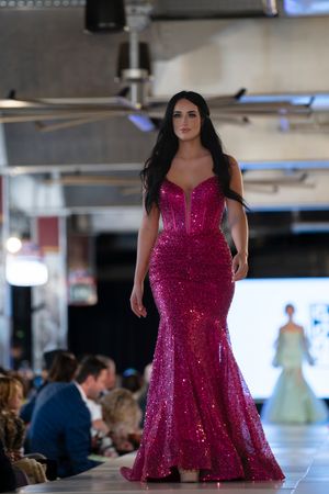 Model walks runway in sparkly magenta cocktail dress during fashion show.