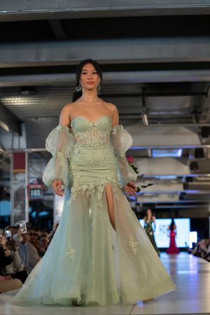 An elegant mint green mermaid gown with puffy sleeves and lace details shown on a fashion catwalk.
