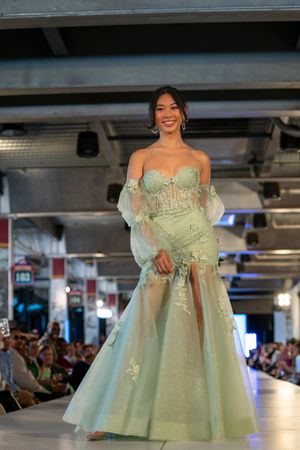 Mint green tulle gown with embellishments displayed on illuminated fashion runway.