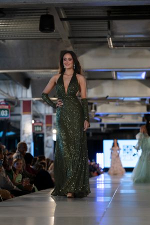 Sparkling emerald green evening gown displayed on illuminated runway during fashion show.