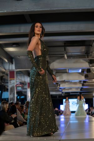 Sparkling emerald green evening gown being showcased on illuminated fashion runway.
