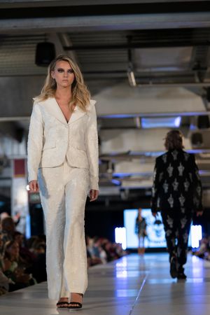 Crisp white pantsuit ensemble being showcased on brightly lit fashion catwalk.