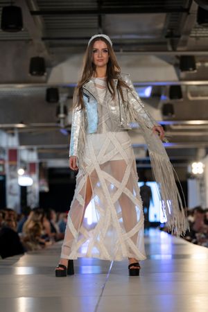 Fashion model showcases white fringed avant-garde outfit on illuminated runway.