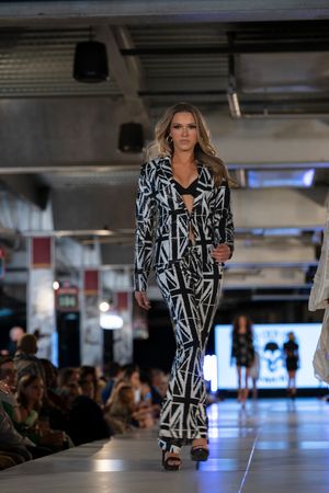 Model showcases black and white geometric print blazer on illuminated catwalk.