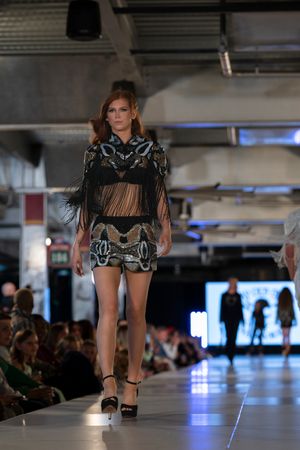 Model walks runway in black fringe detailed mini dress with embellishments.