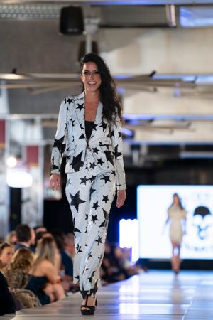 Model presents black and white star-patterned suit on illuminated catwalk.