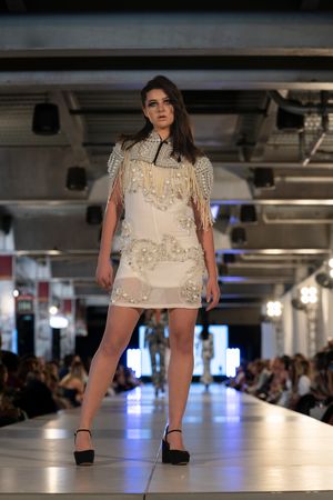 Short beige dress with crystal embellishments and fringe details presented on catwalk.