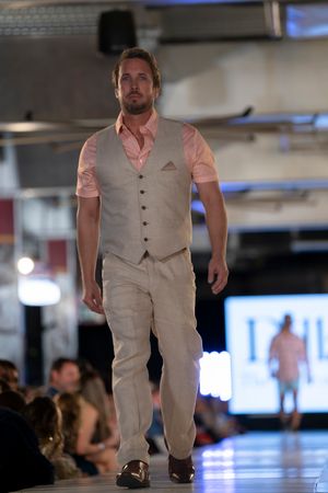 Model wearing light beige vest and pants walks down illuminated runway.