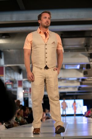 Model wearing beige vest and pants ensemble walks down fashion runway.