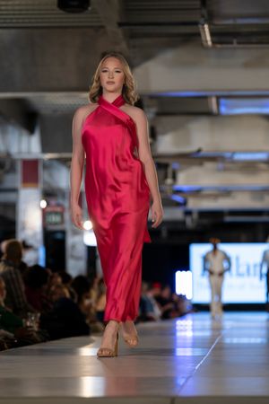 Fashion model walks barefoot in flowing red satin dress on illuminated catwalk.