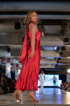 Red satin cocktail dress with ruffled details displayed during fashion show.