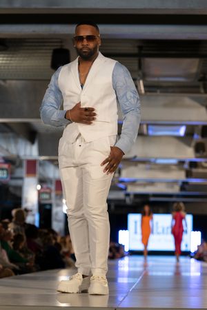 Model showcases crisp white suit with light blue dress shirt on illuminated catwalk.