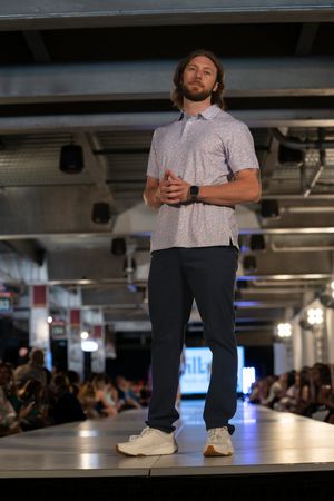 Model in casual attire with white t-shirt and dark pants walks runway.