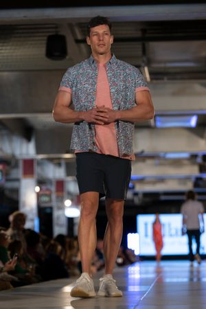 Model presents floral print shirt and dark shorts combination on fashion runway.