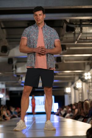 Model showcases casual summer outfit with floral print shirt and shorts on illuminated catwalk.
