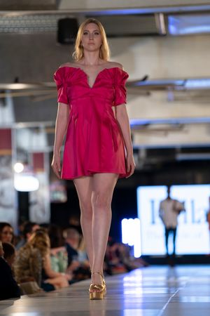 Bright red ruffled top design featured on illuminated fashion show runway.