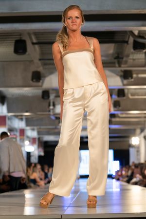 Model showcases elegant cream-colored wide-leg jumpsuit on illuminated catwalk.