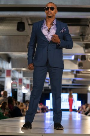 Model struts down catwalk wearing navy blue suit with pocket square.